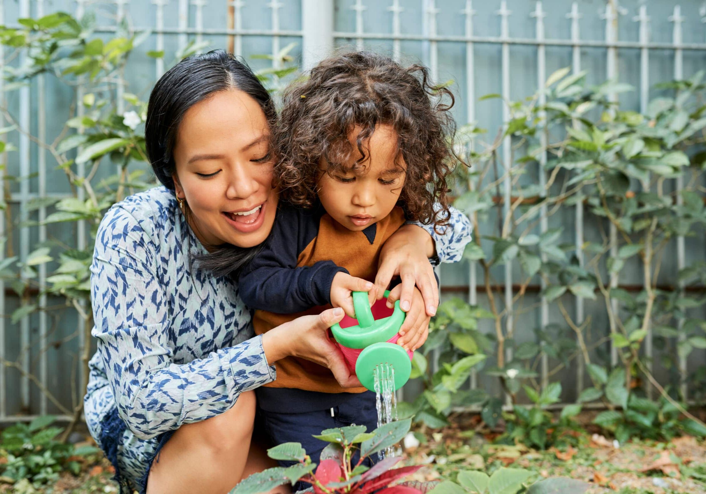 Joyful mother and son enjoying watering flowers in garden