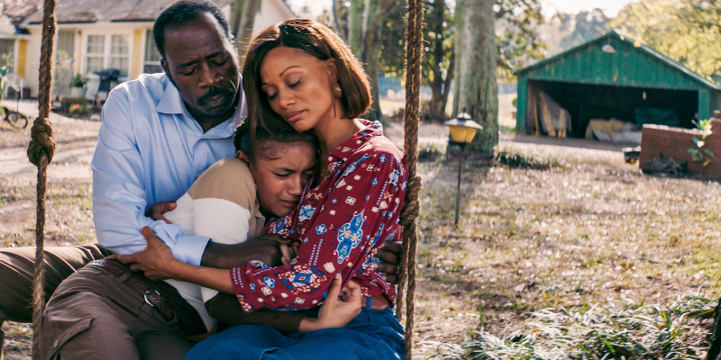 mother and father hugging tearful child on a swing outdoors
