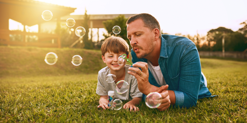 child and father blowing bubbles at sunset in the grass