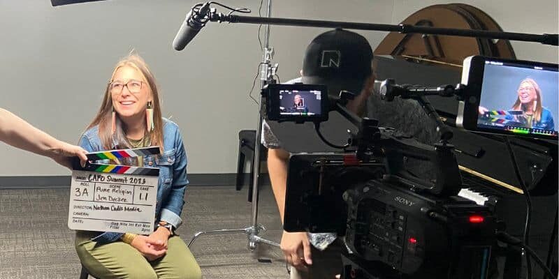 behind the scenes photo of smiling female with a microphone and camera set up to film