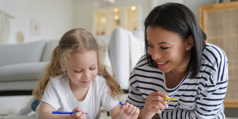Adult female sits with child coloring in a book