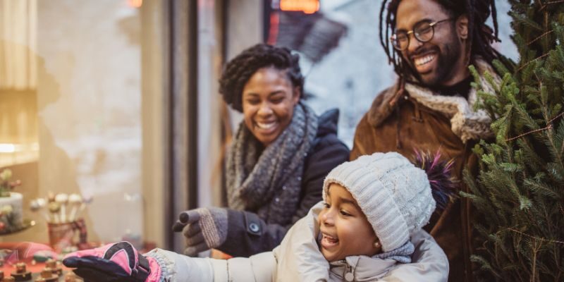 family with christmas tree outdoors window shopping