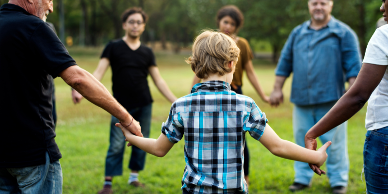 child stand in a circle with various other adults standing together holding hands