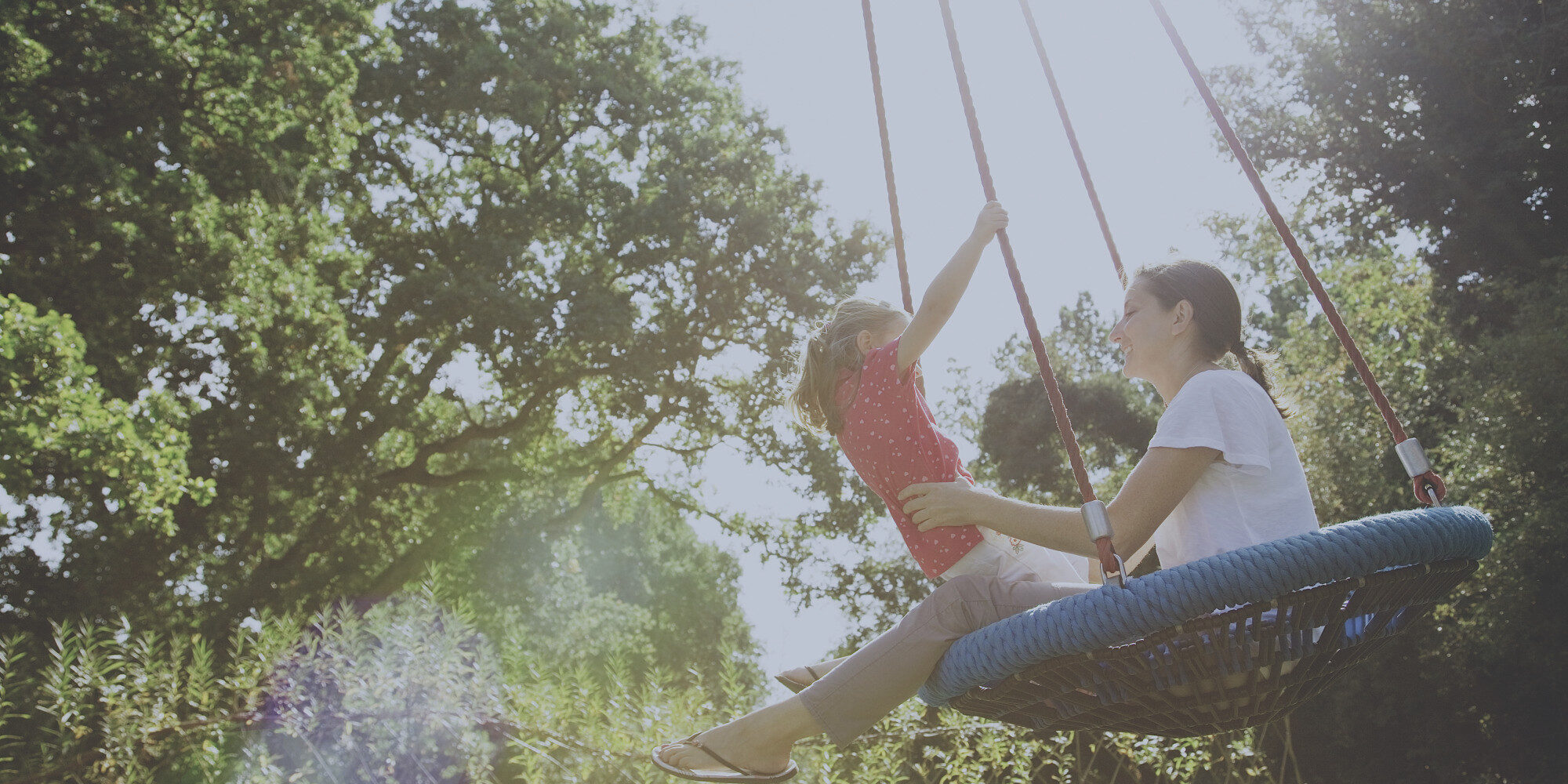 Mother and daughter on swing in sunny park